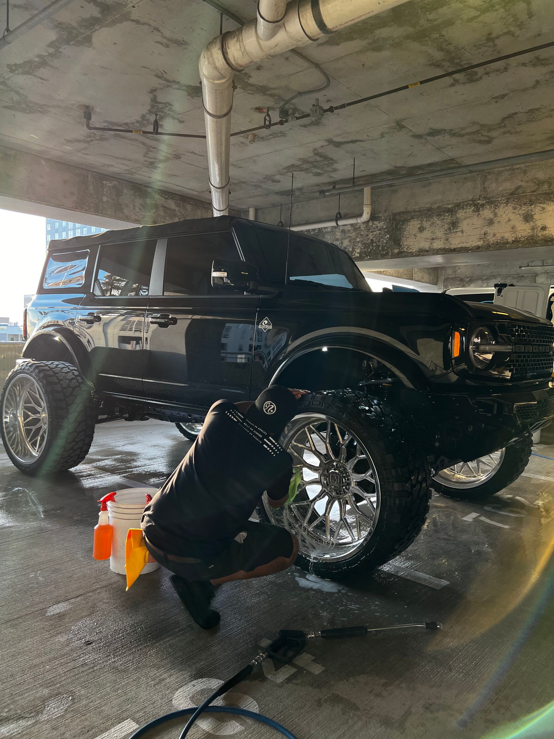 A black jeep is being washed under a bridge in a parking garage.