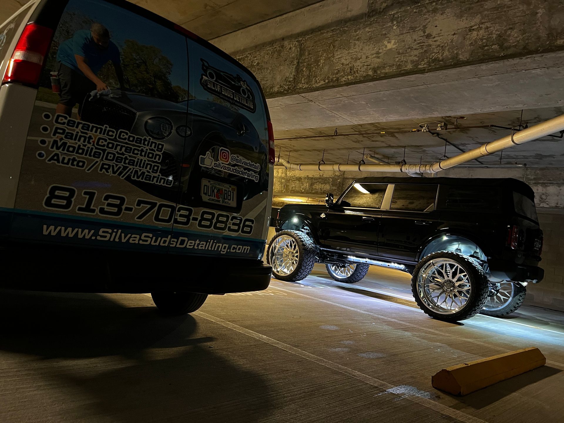 A black suv is parked next to a van in a parking garage.