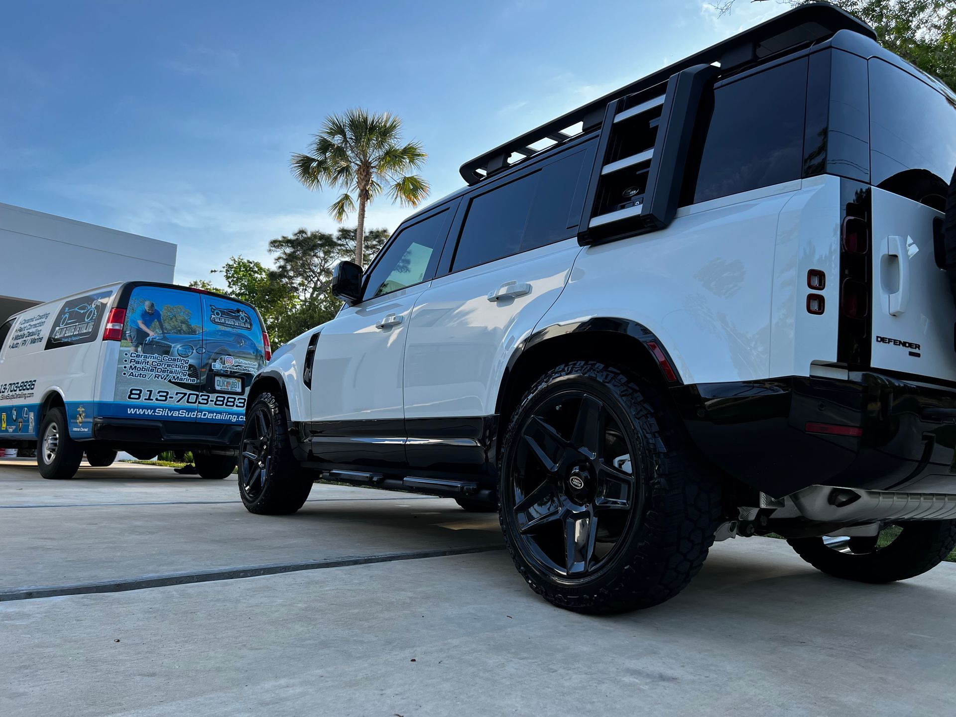 A white suv with a ladder on the back is parked next to a white van.