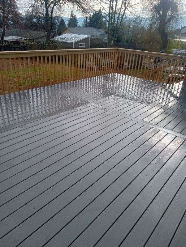 Wet gray deck with wooden railing in a backyard.