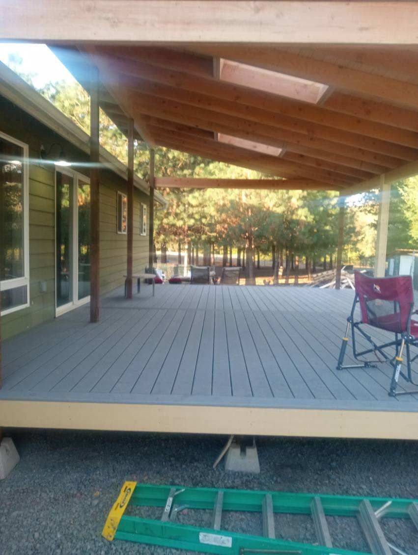 Covered wooden deck with a gray floor, extending from a green house.