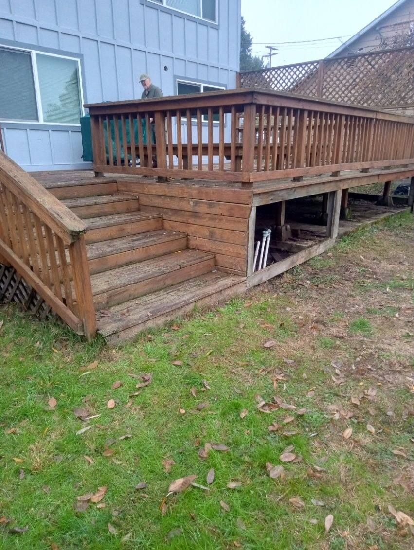 Wooden deck with stairs leading to a raised platform. A person stands on the deck. Green grass surrounds it.