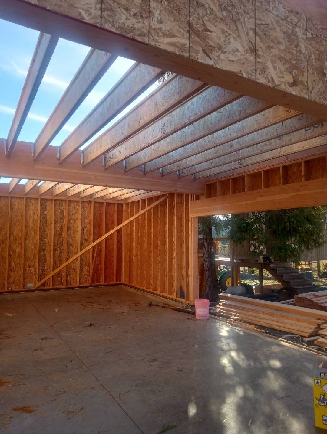 Interior view of a building under construction. Wooden beams and framing, concrete floor. Outdoor view through doorway.