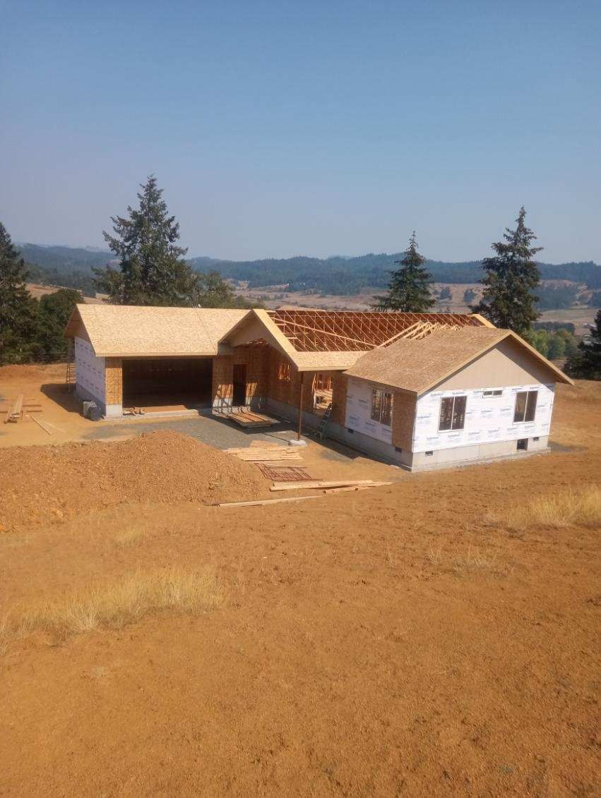 New house under construction with unfinished roof in a field on a sunny day.