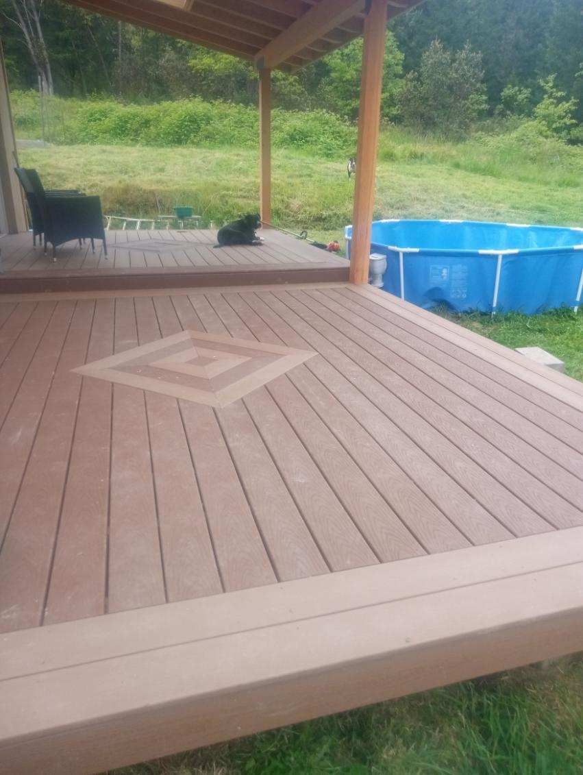 Wood deck with embedded design, covered porch, and above-ground pool in a grassy yard.