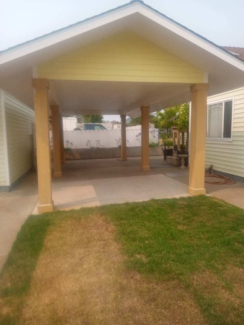 Yellow carport with tan columns, a concrete floor, and patches of grass in front.