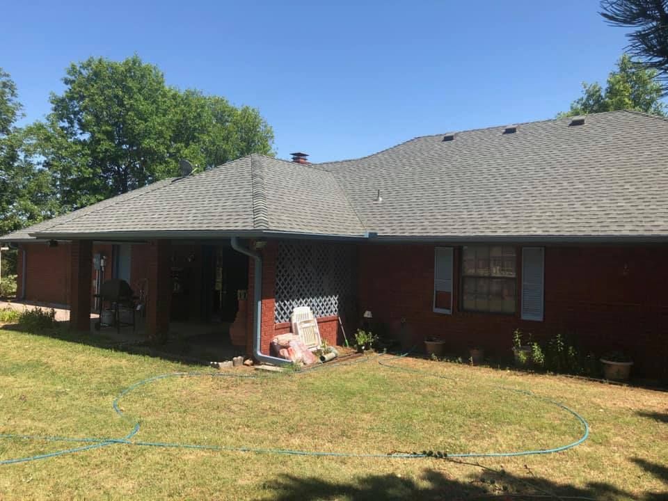 A red brick house with a gray roof is sitting on top of a lush green lawn.