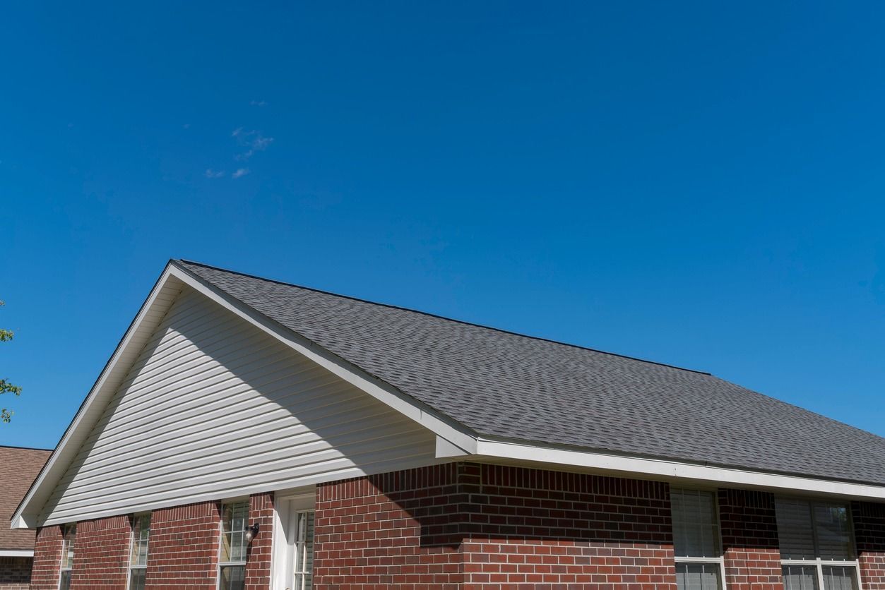 A brick house with a gray roof and a blue sky in the background.