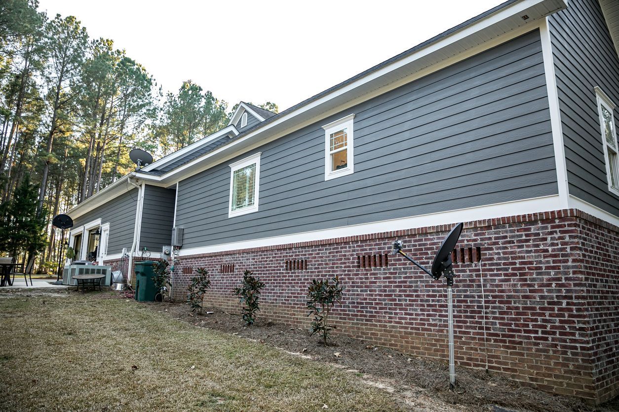 The side of a house with a brick foundation and a gray siding.