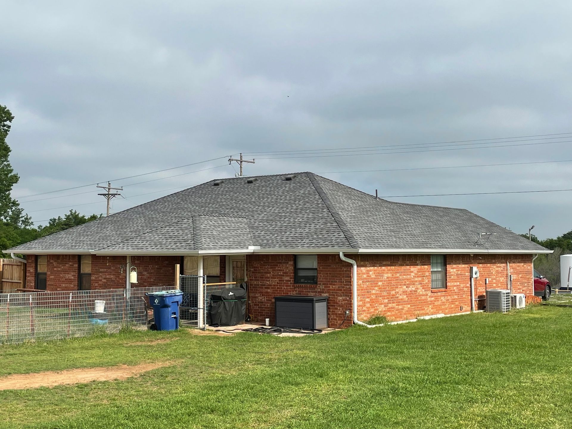 A brick house with a gray roof is sitting on top of a lush green field.