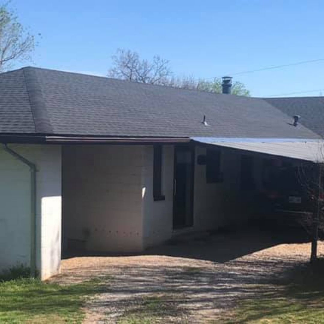A white house with a black roof and a car parked in front of it.