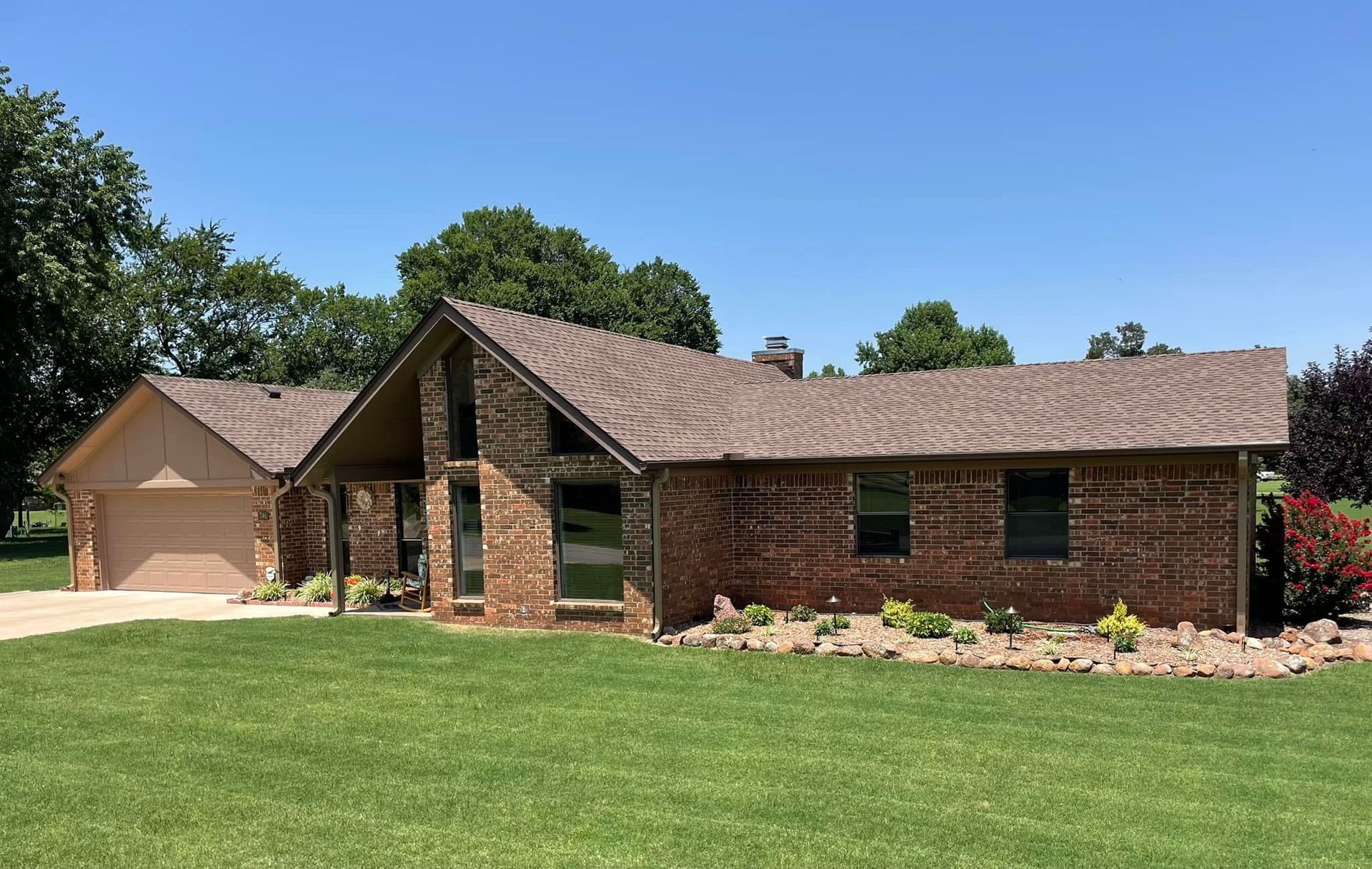 A brick house with a brown roof is sitting on top of a lush green field.