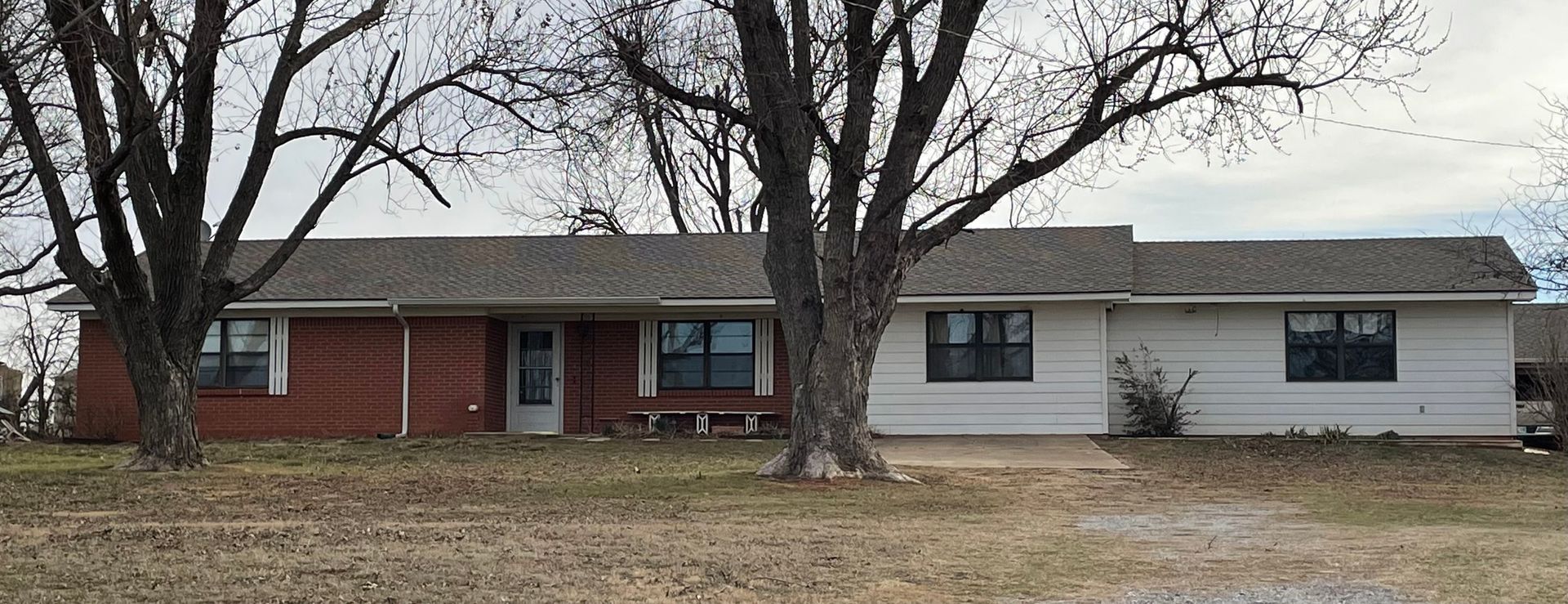 A brick house with a white siding and a gray roof is surrounded by trees.