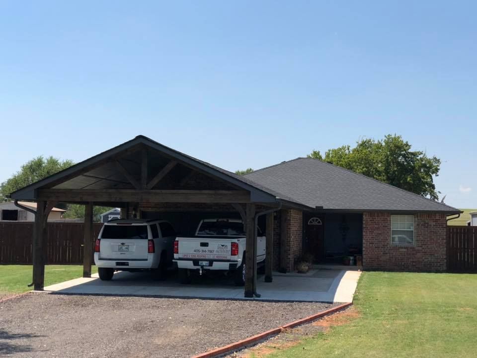 Two cars are parked under a carport in front of a house.