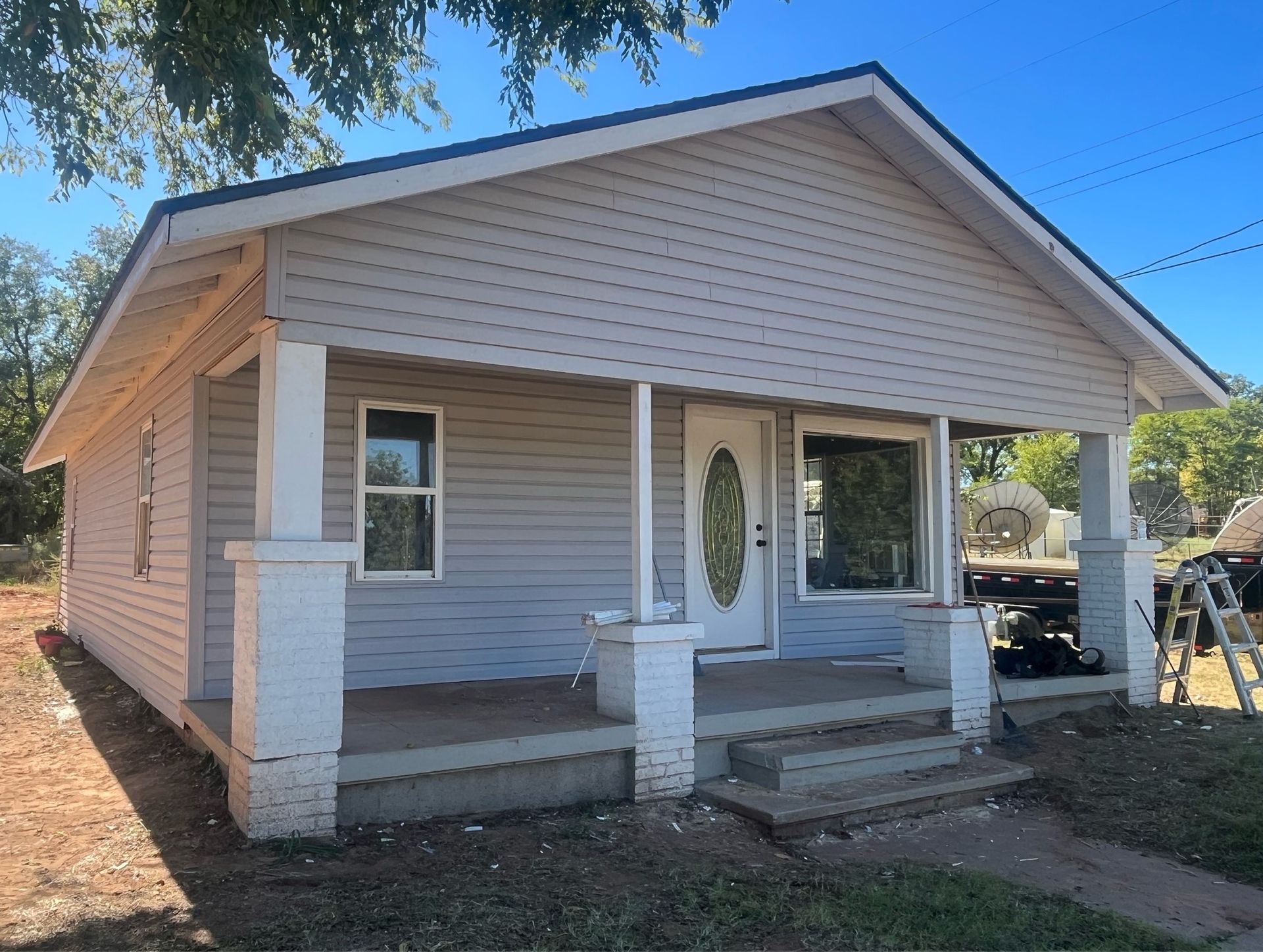 A small house with a porch and a ladder in front of it.