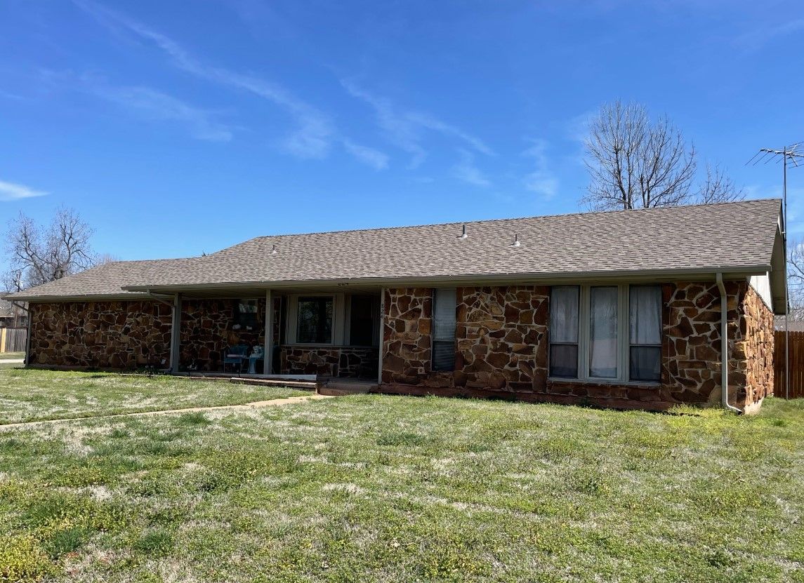 A brick house with a brown roof and a large lawn in front of it.