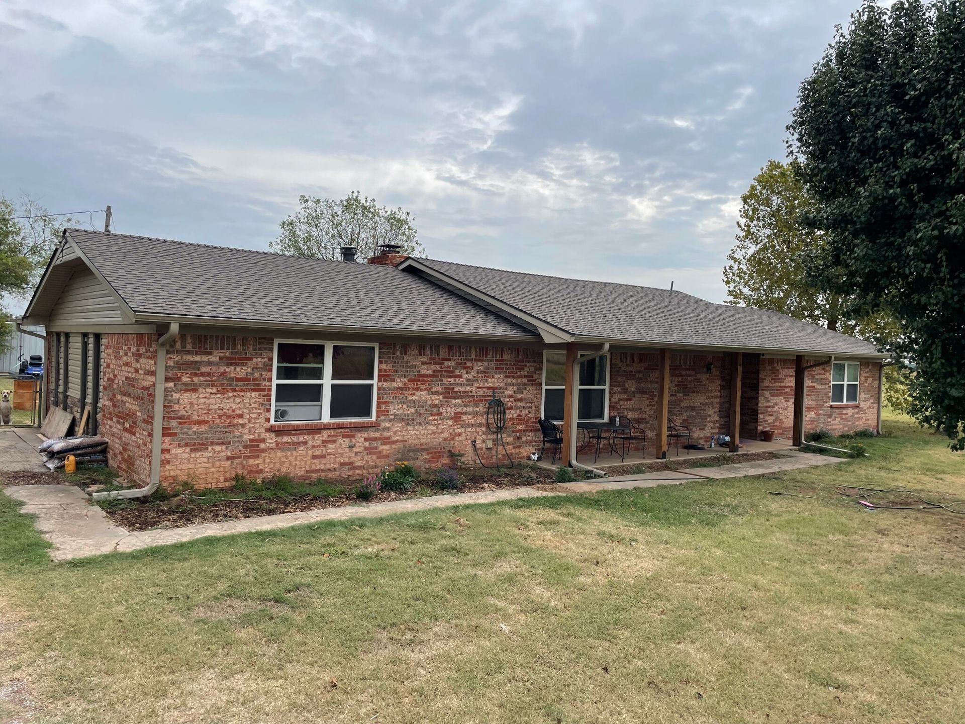 A large brick house with a gray roof is sitting on top of a lush green field.