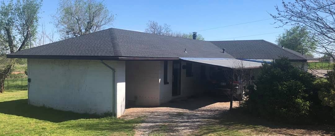 A small white house with a black roof is sitting in the middle of a grassy field.
