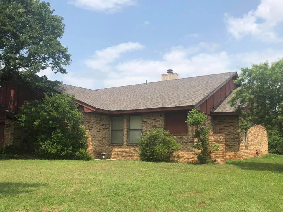 A large brick house with a gray roof is sitting on top of a lush green field.