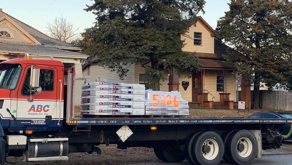 A flatbed truck with abc written on the side is parked in front of a house.
