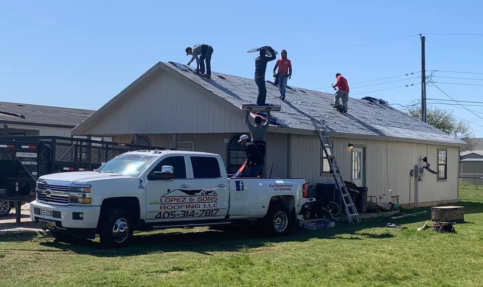 A white truck is parked in front of a house while people work on the roof.