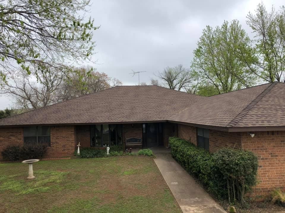 A brick house with a brown roof and a bird bath in front of it.