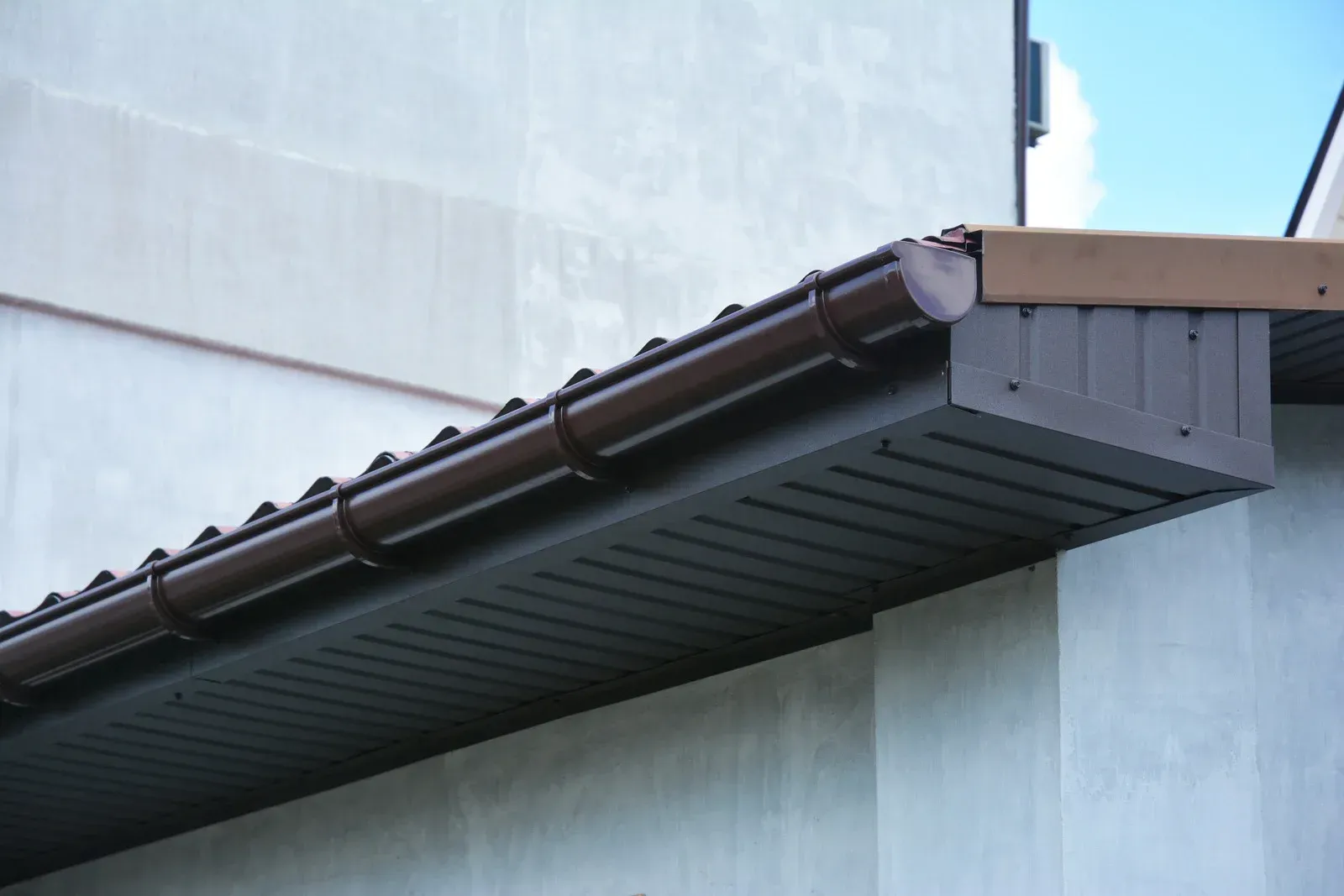 Brown rain gutter along a building's edge, with a brown soffit and a pale wall.