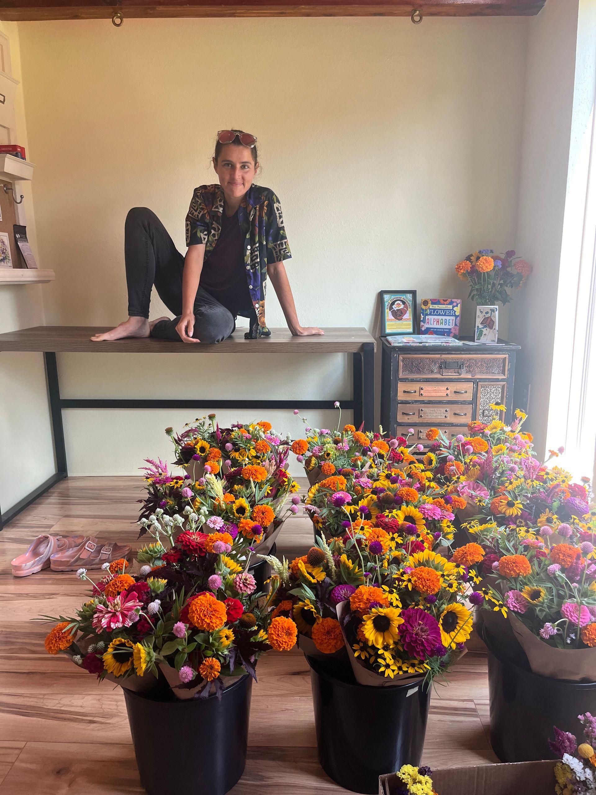 Marine in the Tiny Shop sitting on the table with lot of flower bouquets in buckets on the ground