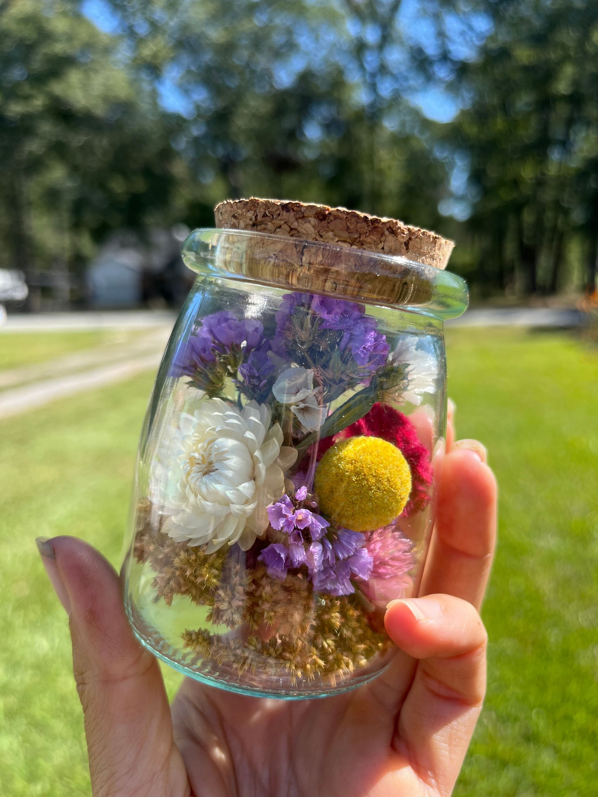 A person is holding a jar filled with dried flowers.