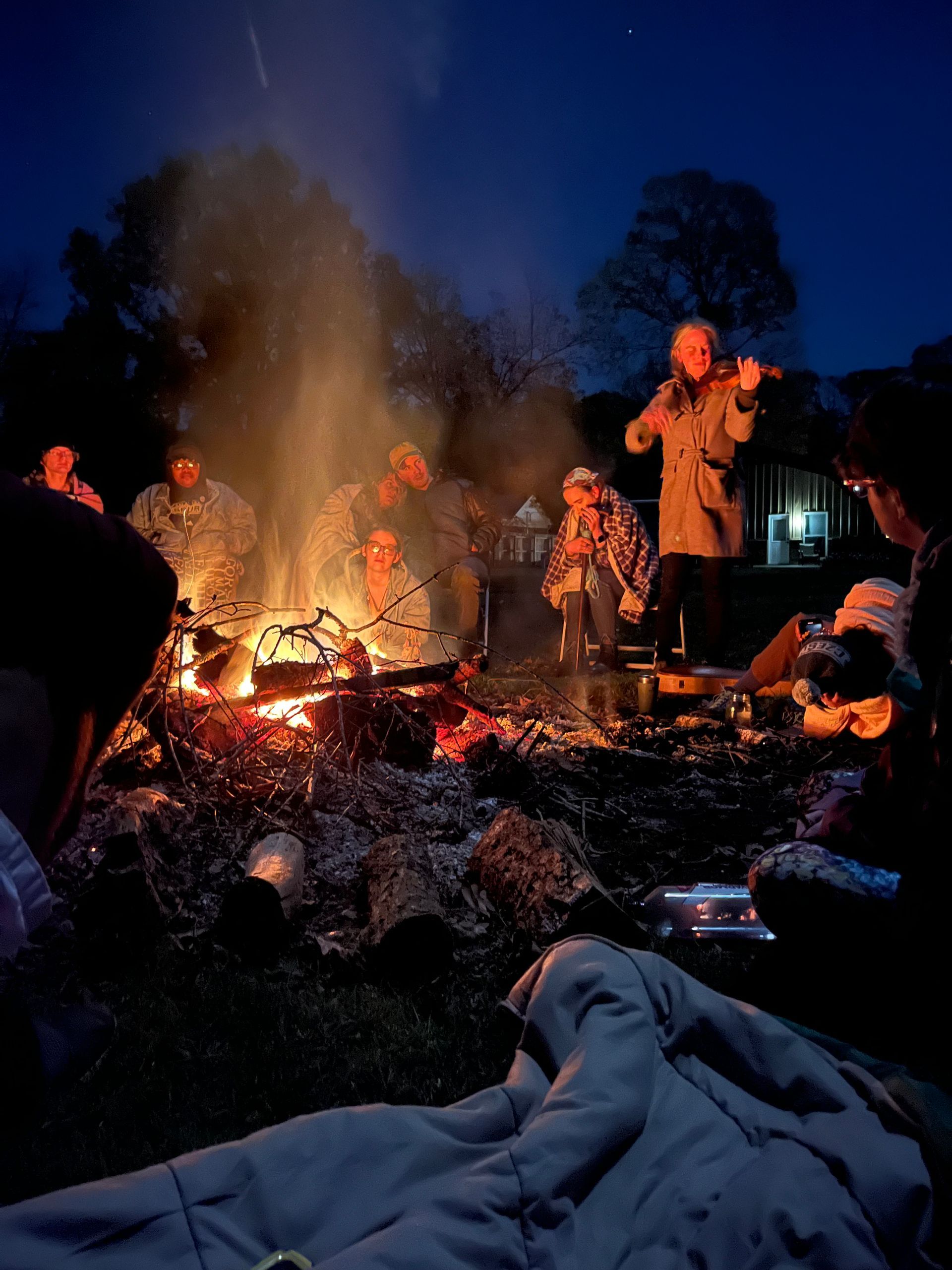 People listening to the violin around a bonfire in the night at the farm