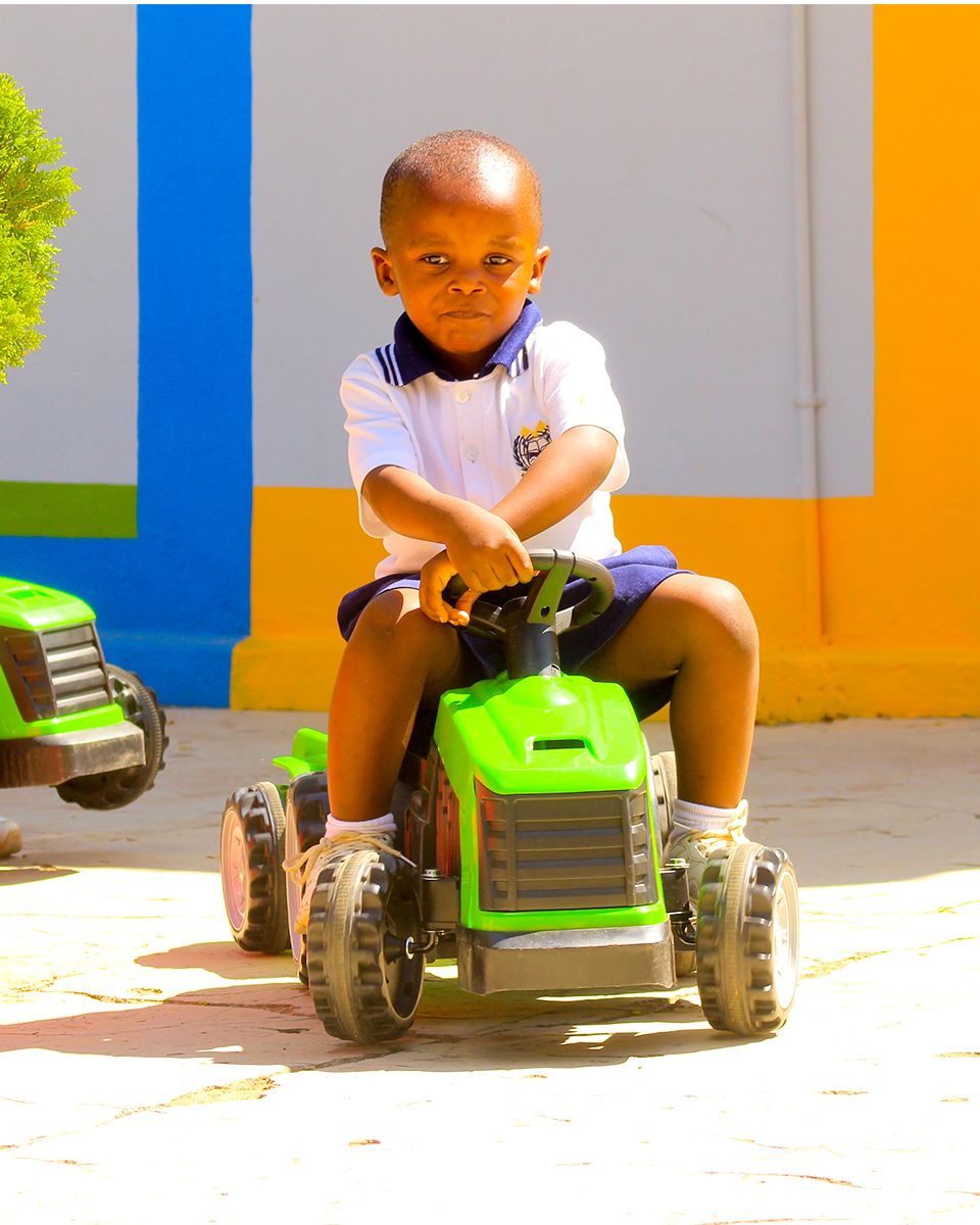 A young boy is sitting on a green toy tractor.