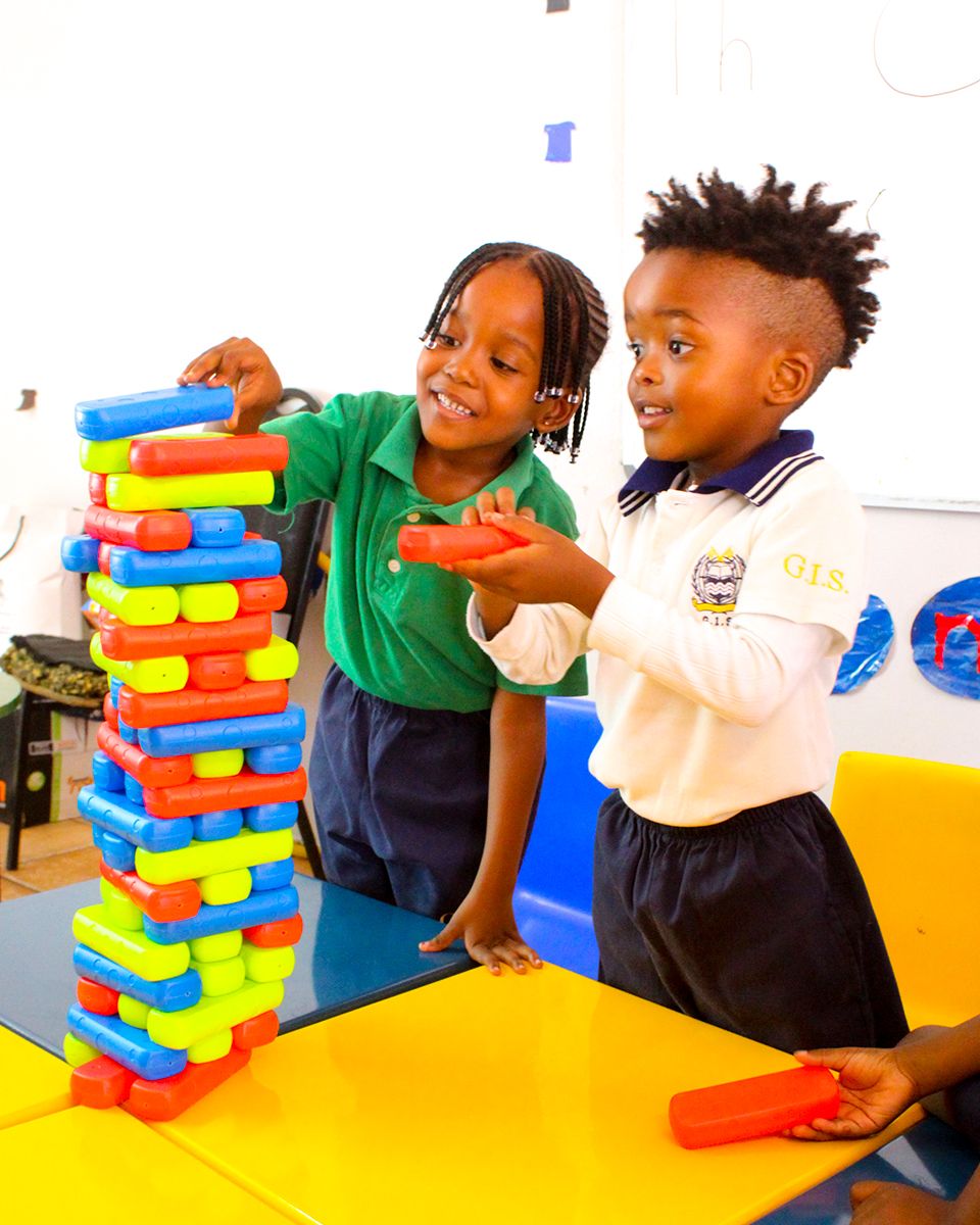 Two children are playing with a stack of colorful blocks.
