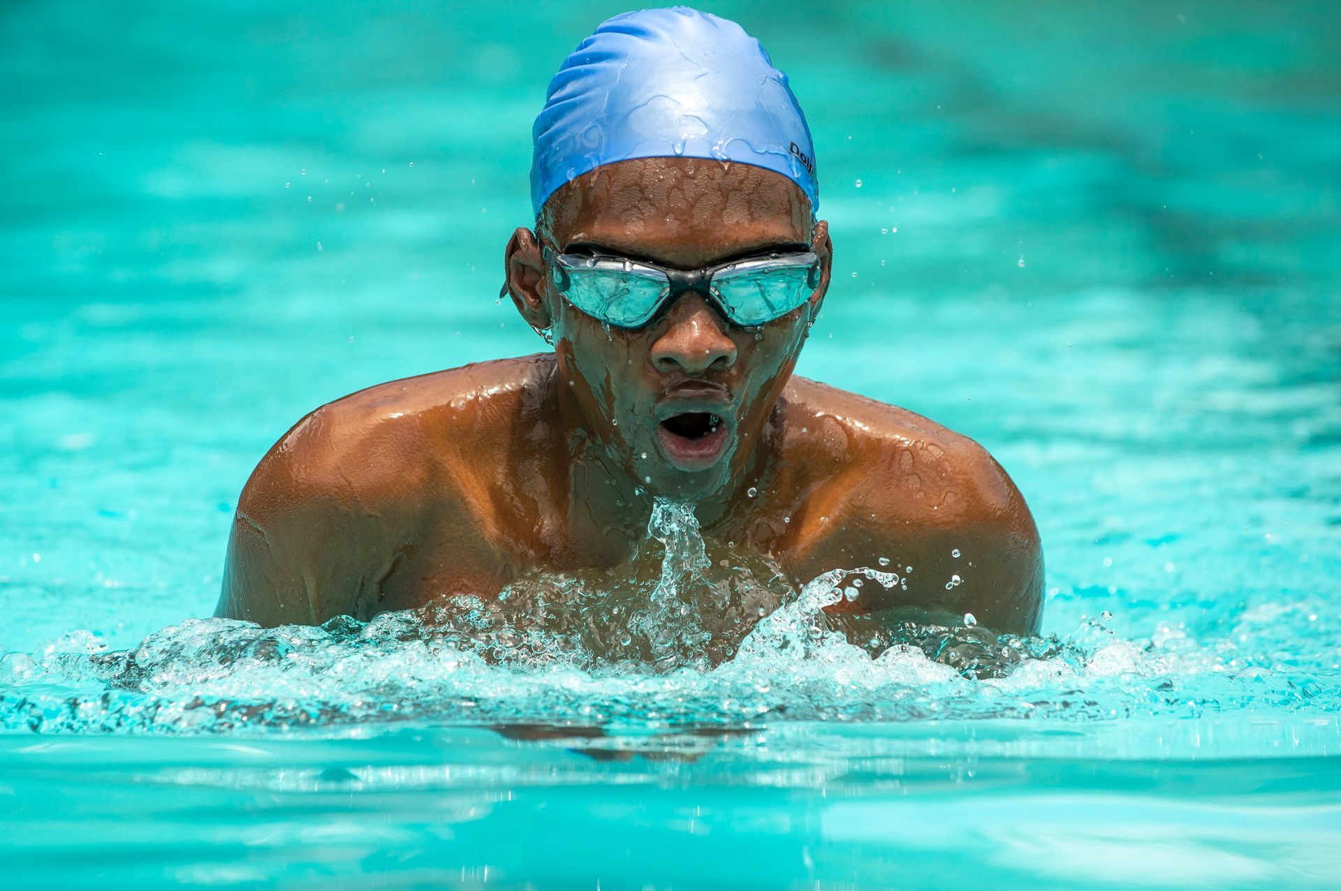 A man is swimming in a pool wearing a blue cap and goggles.