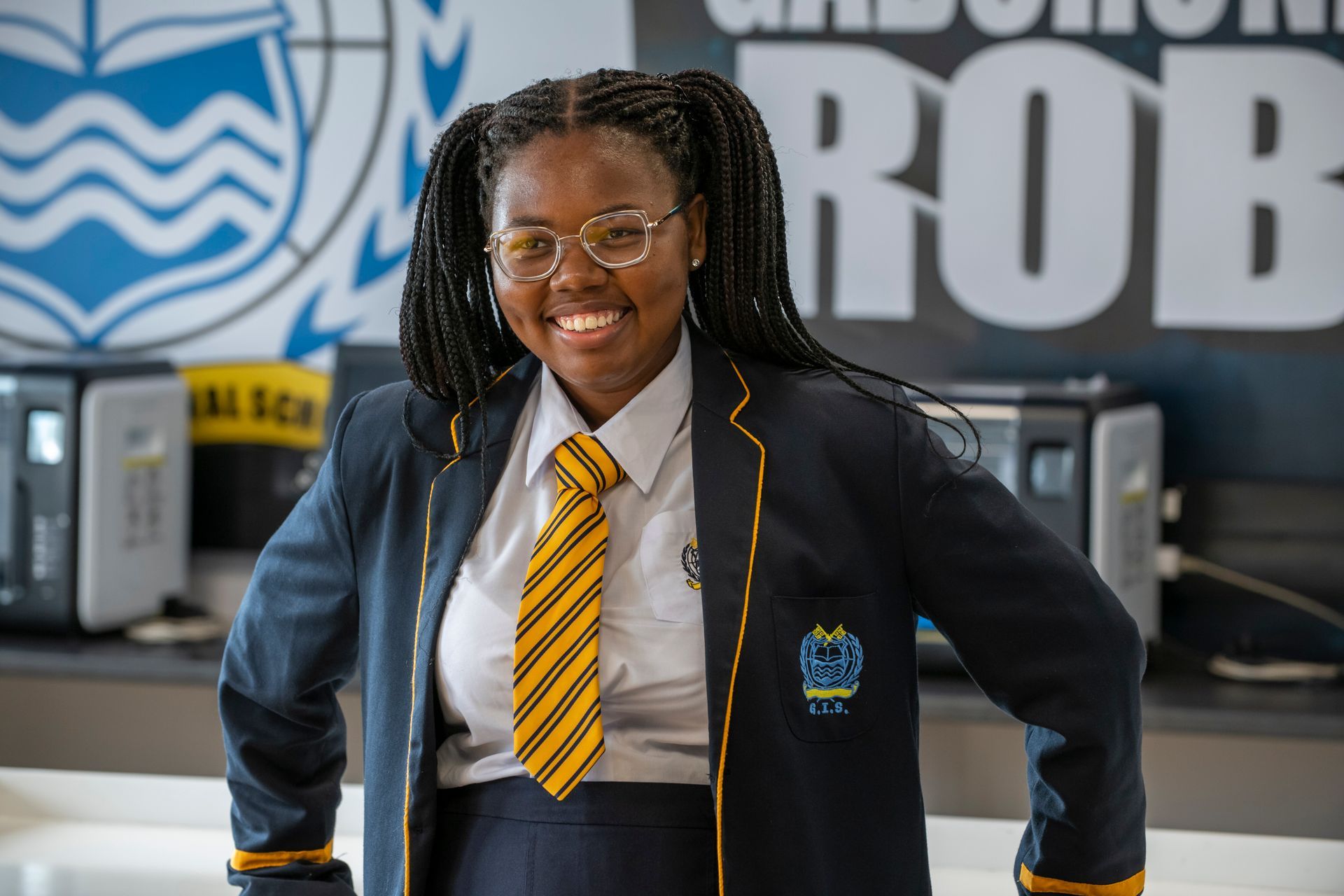 A young woman in a school uniform and tie is smiling.