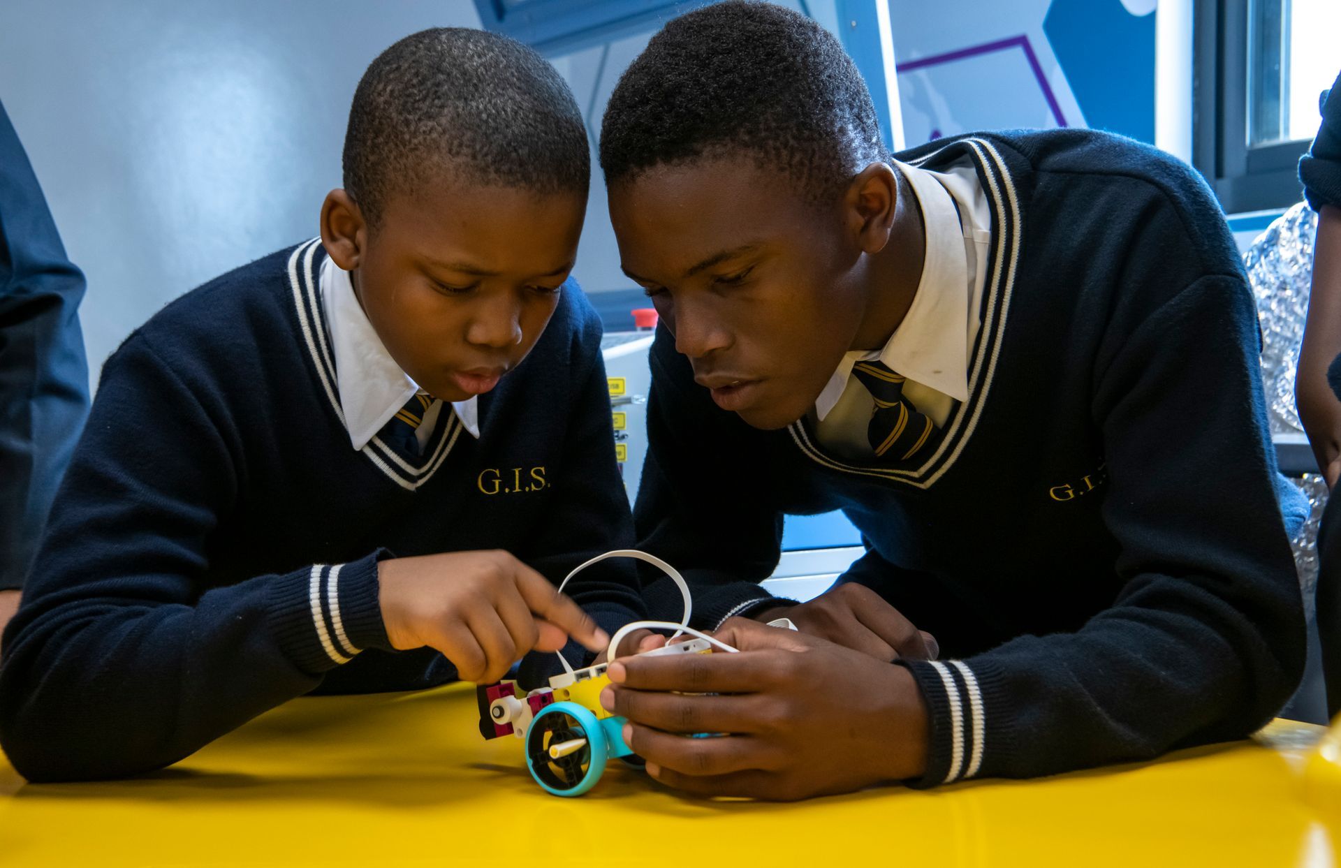 Two young boys are playing with a toy car on a yellow table.