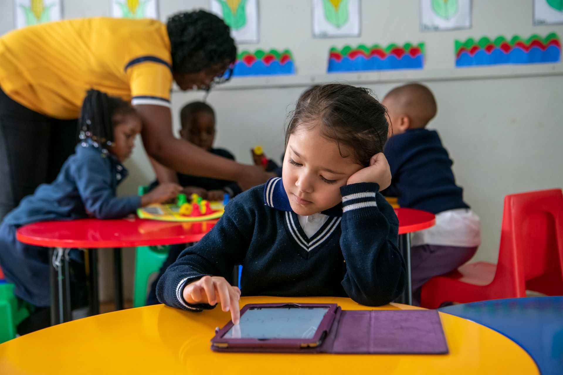 A young girl is sitting at a table using a tablet computer.