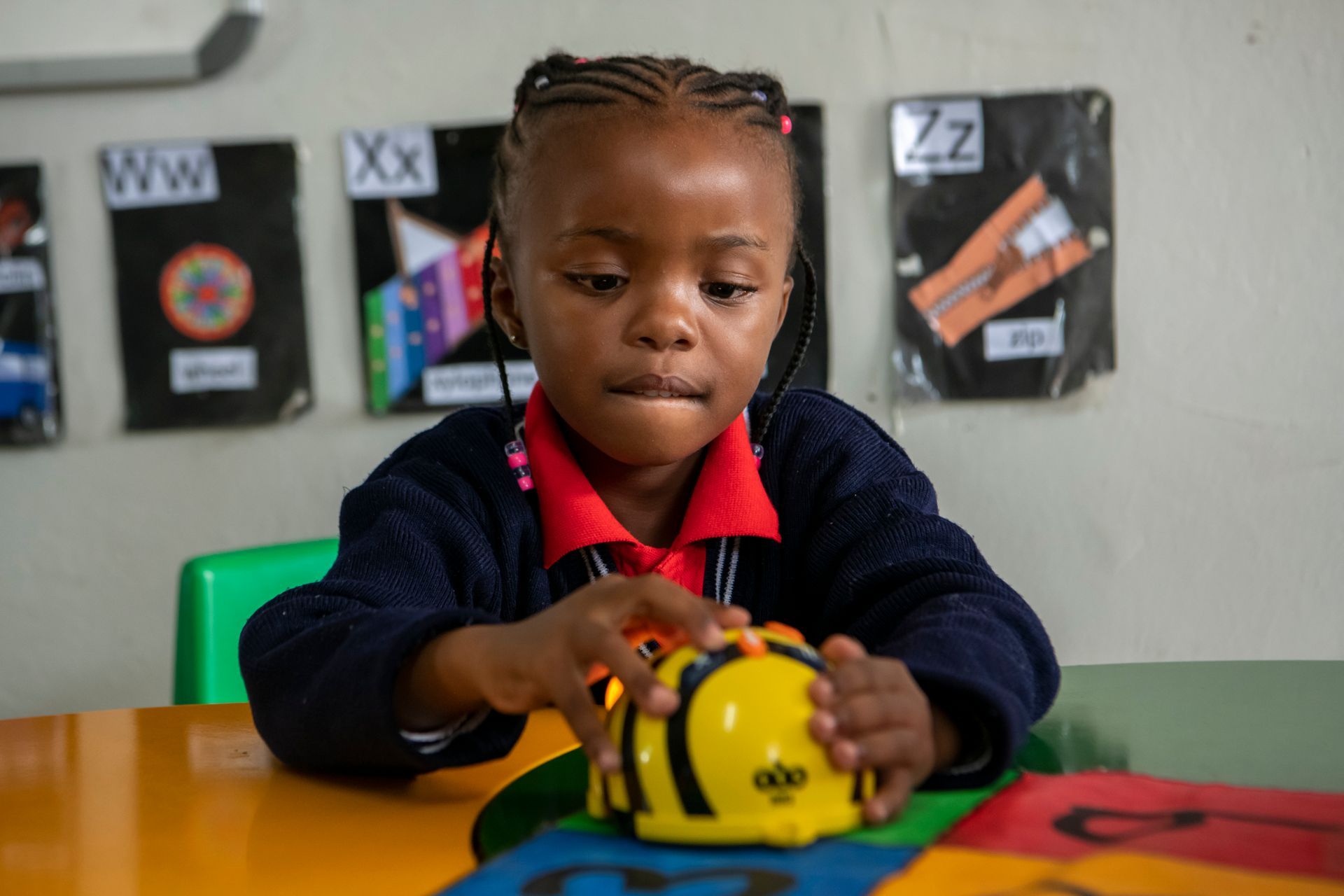 A young girl is sitting at a table playing with a toy robot.