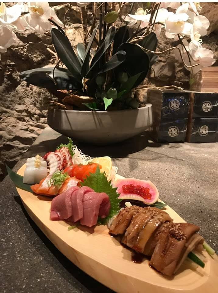 Sushi platter with assorted nigiri and rolls on a wooden board beside a potted orchid