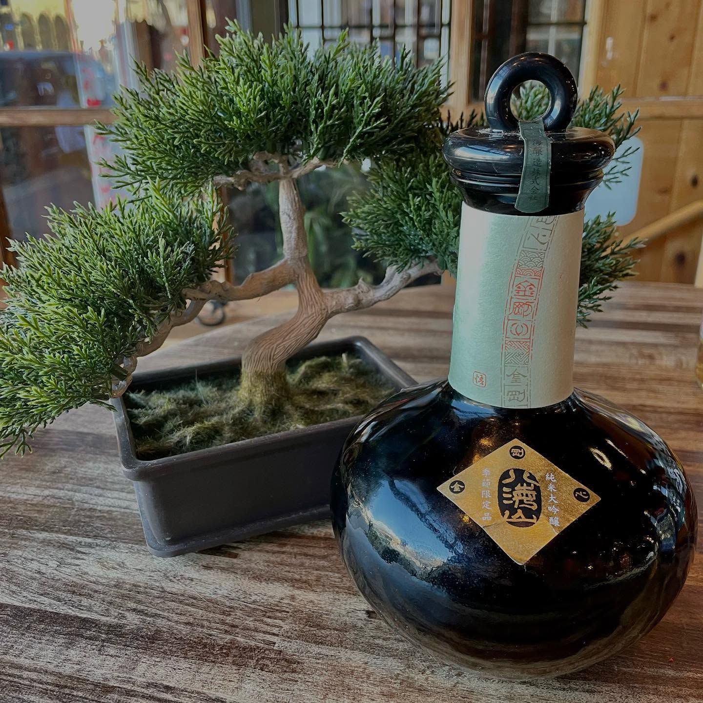 A bonsai tree beside a black decorative bottle on a wooden table.