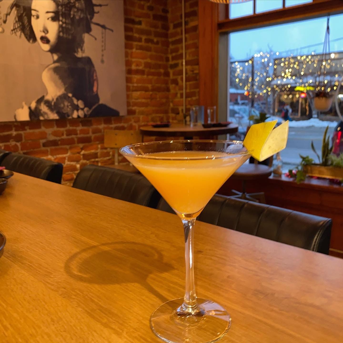 Cocktail with pineapple garnish on a wooden bar in a cozy brick-walled lounge, window lights in the background