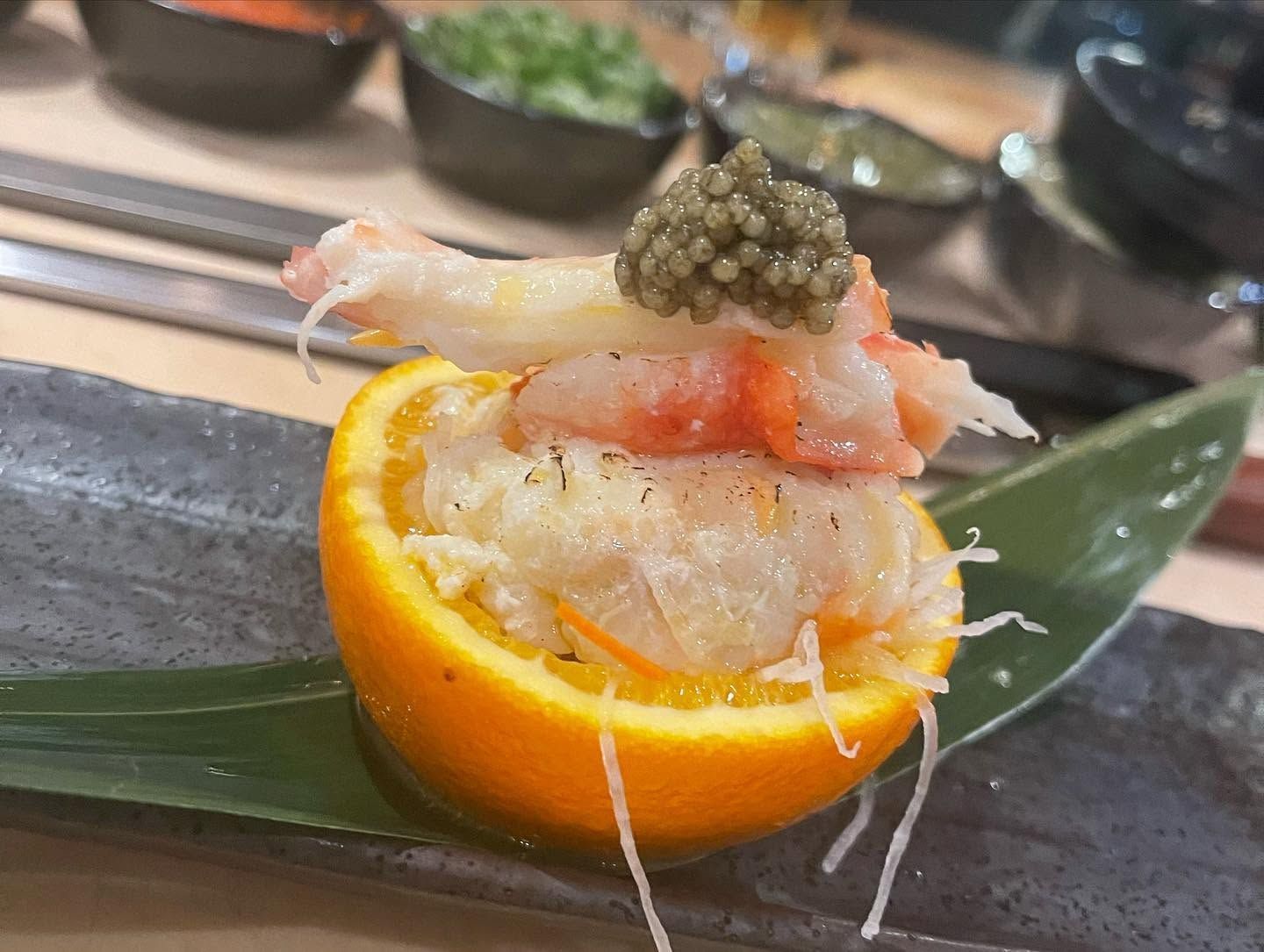 Seafood appetizer in an orange half, topped with crab, shrimp, and caviar on a plate