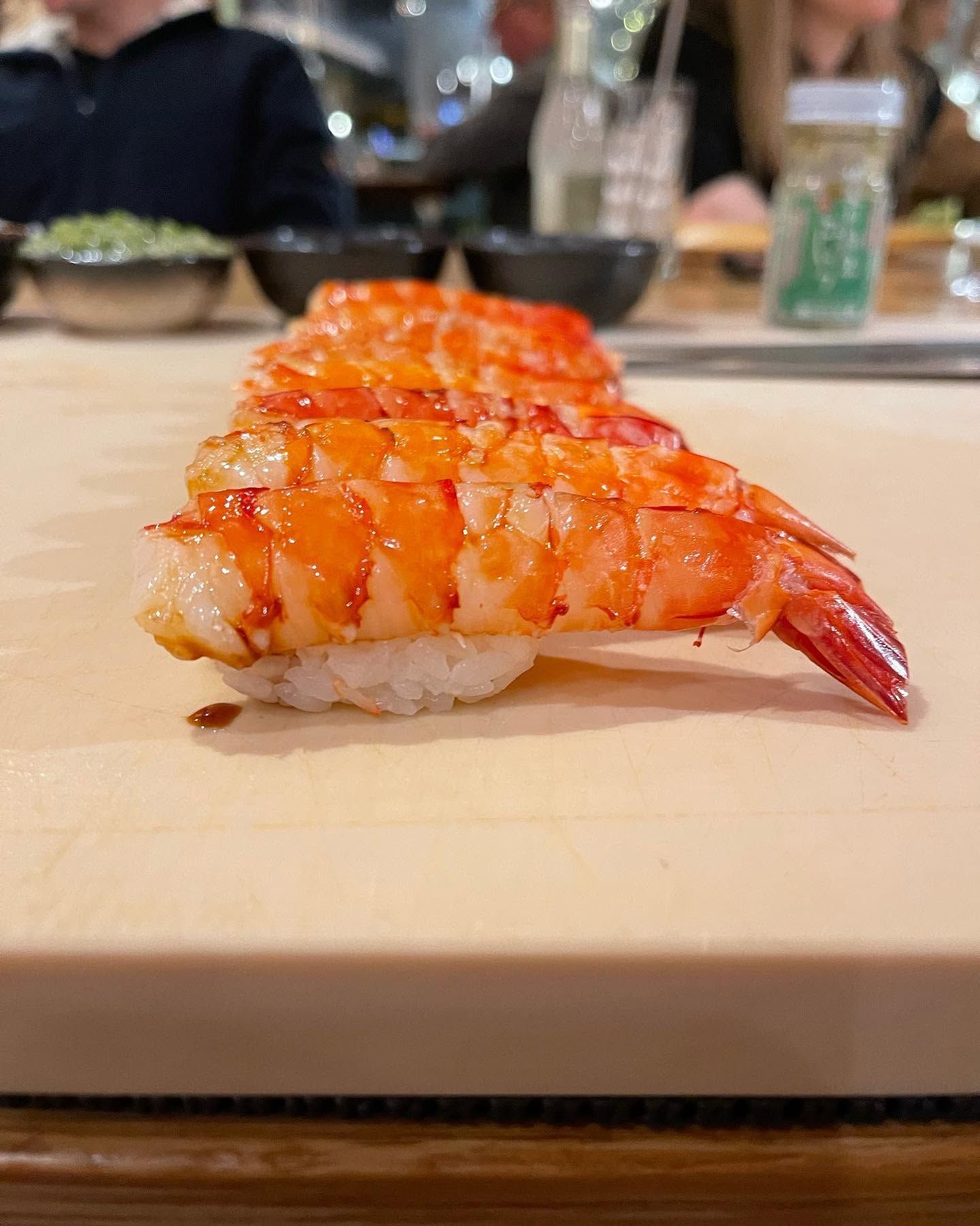 Glazed sushi nigiri with orange shrimp topping on a wooden board, restaurant background.