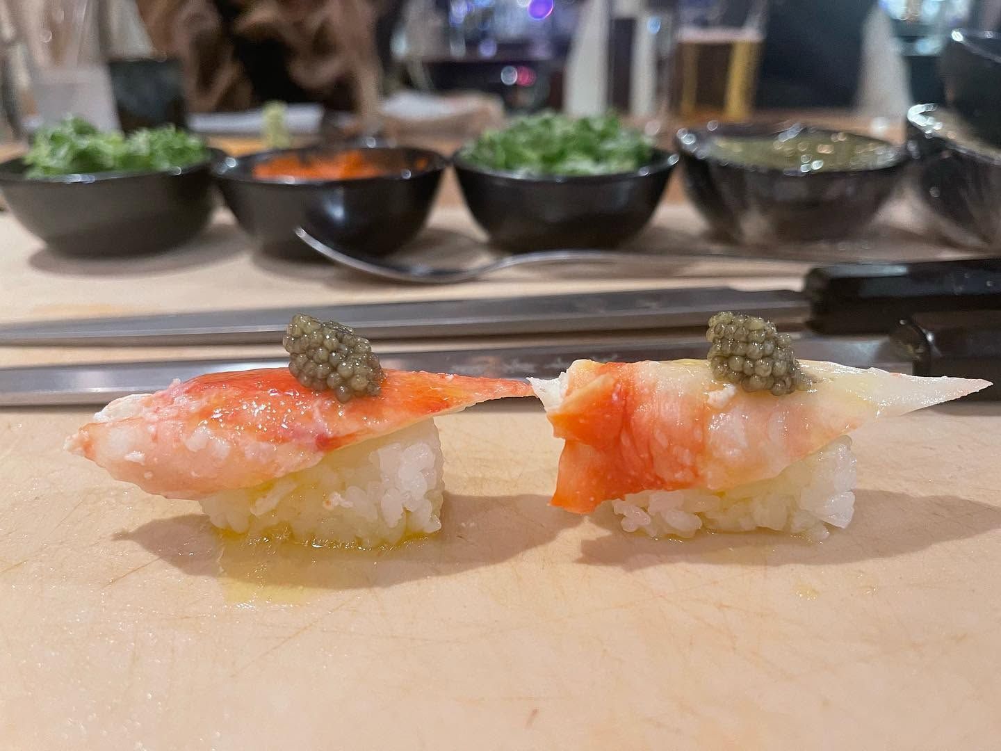 Two pieces of sushi on a counter with blurred bowls of food in the background