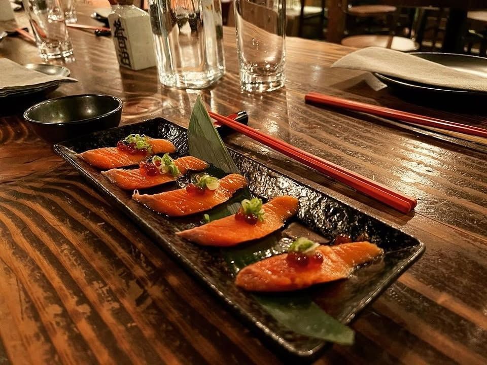 Sushi sashimi plated on a black dish with chopsticks on a wooden restaurant table