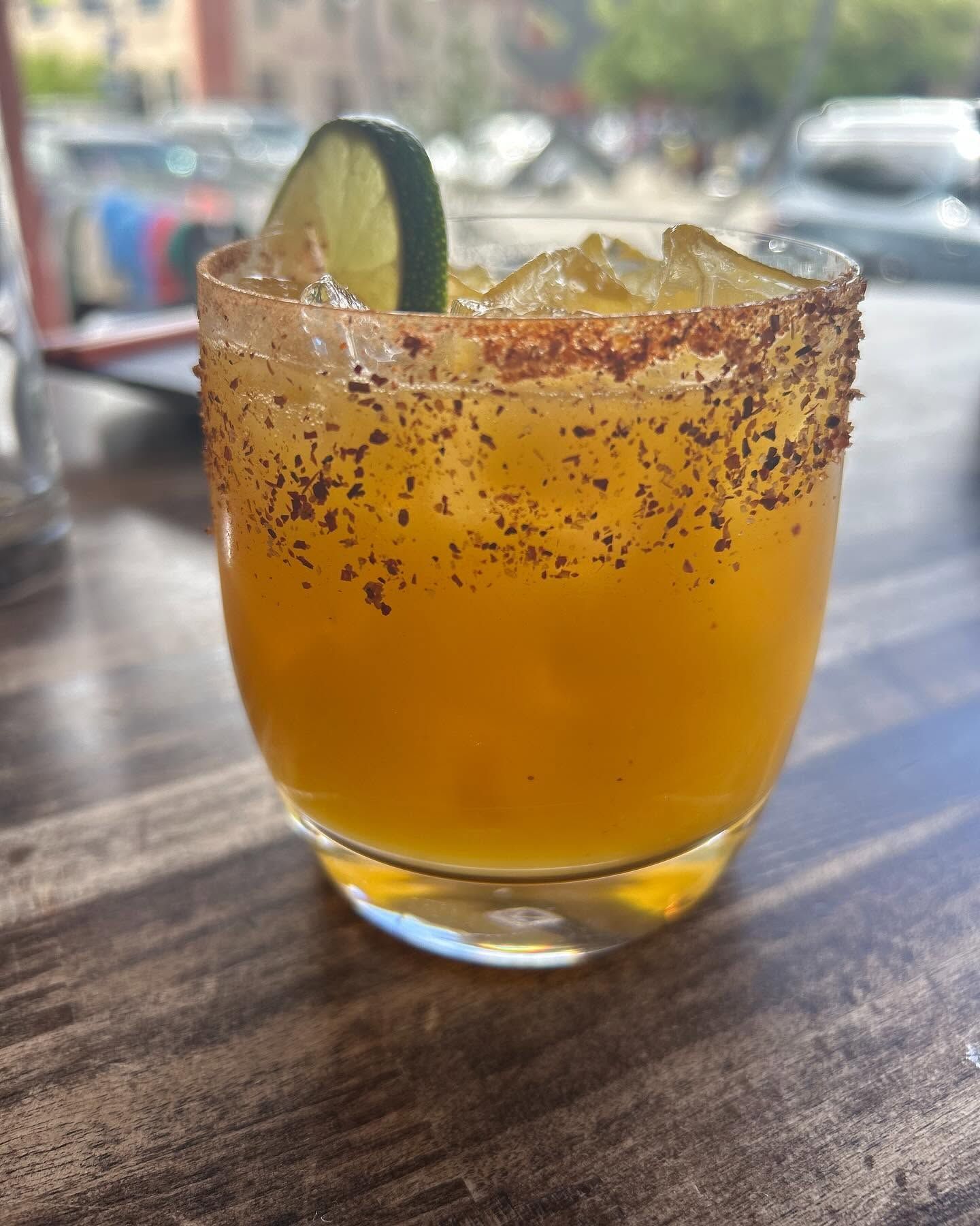 Orange cocktail in a salted-rim glass with a lime slice on a table outdoors.