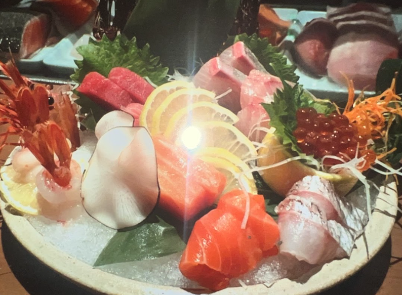 Assorted sushi sashimi arranged in a circular pattern on a black plate with garnish in the center