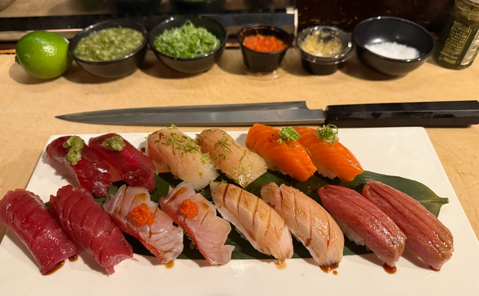 Assorted sushi nigiri platter with lime and small condiment bowls on a restaurant counter