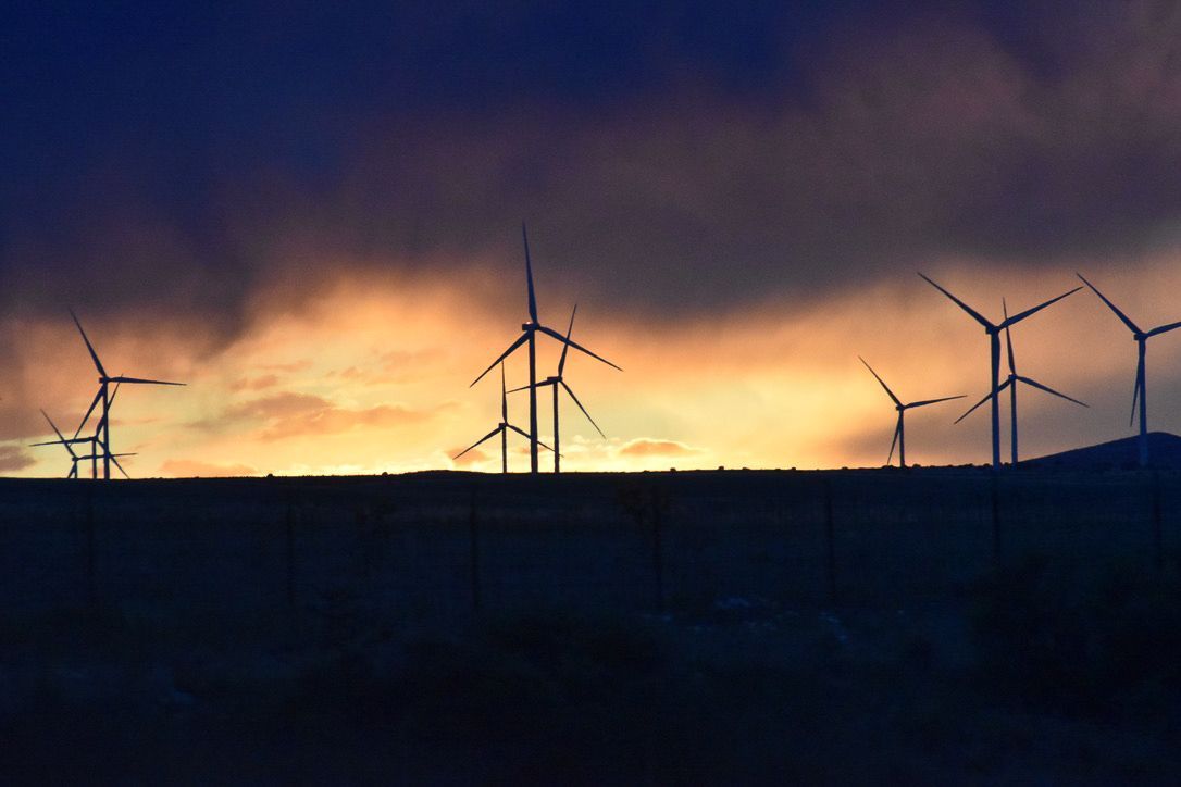 Wind turbines silhouetted against a dramatic sunset sky, in a rural landscape.