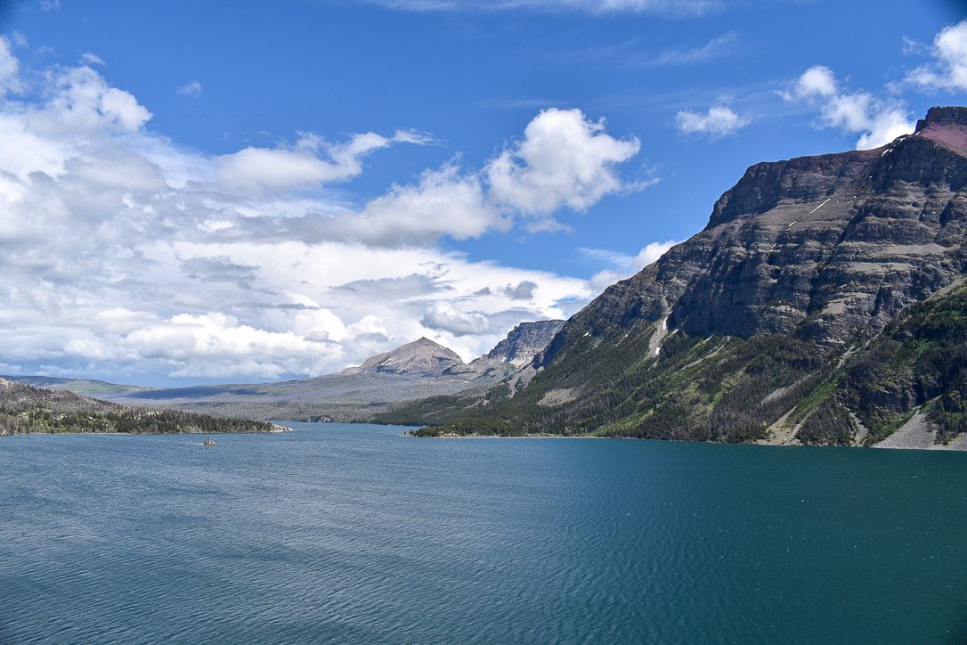 Blue lake with rocky mountains under a partly cloudy sky.