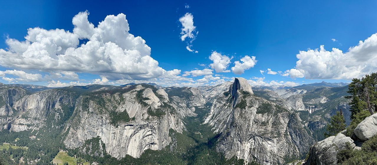 Panoramic view of rocky mountains and green valleys under a blue sky with fluffy clouds.